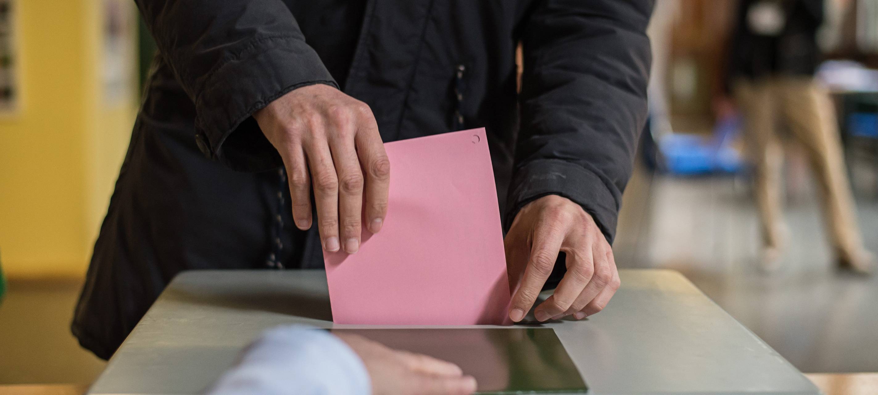 Ein Stimmzettel in einem Umschlag wird in eine Wahlurne eingeworfen.