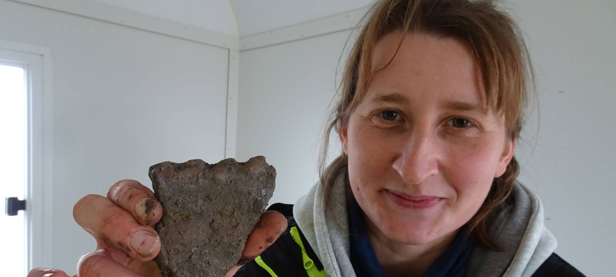 Grabungsleiterin Martha Zur-Schaepers zeigt ein Randfragment eines eisenzeitlichen Gefäßes. Der Rand wurde mit Fingertupfen verziert.