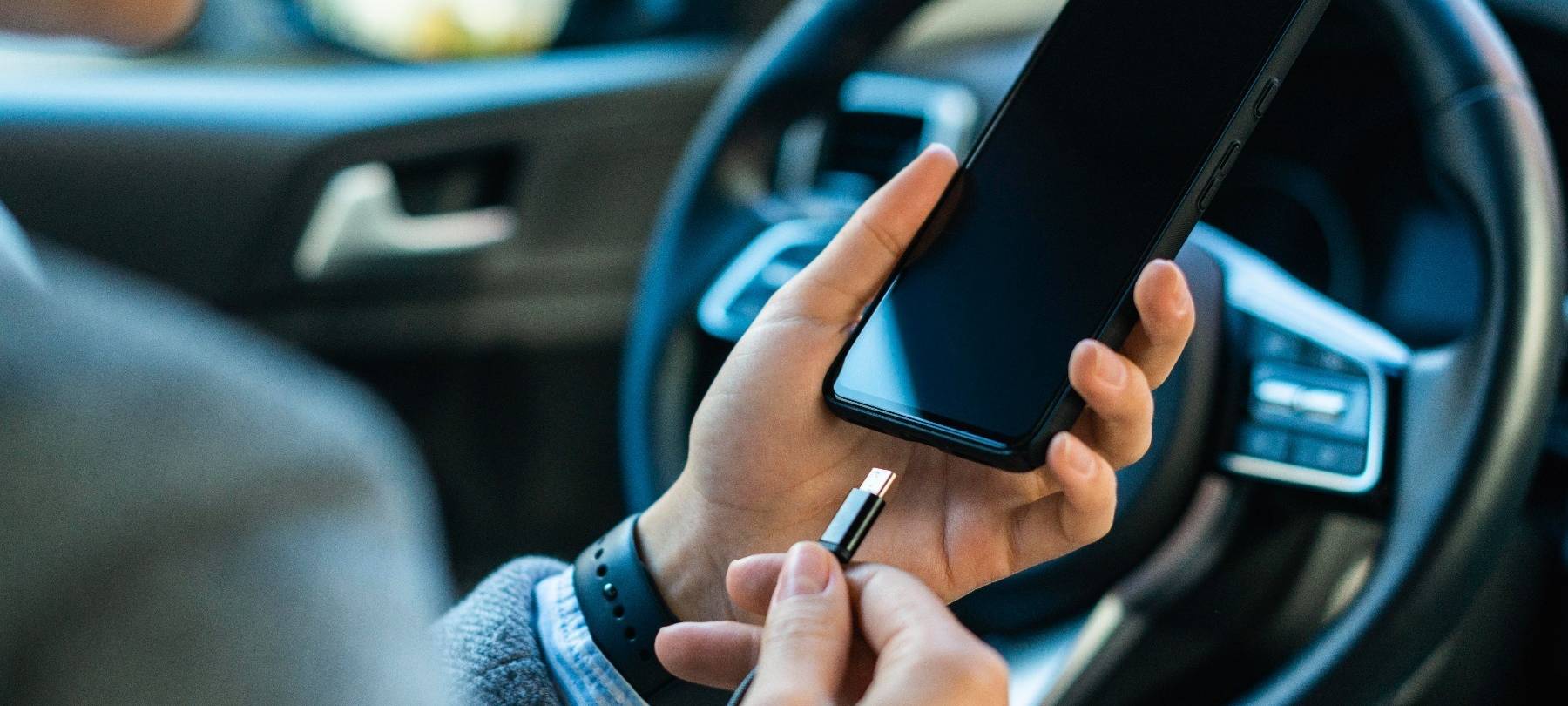 Im Auto wird im Stand ein Handy an ein Ladekabel angeschlossen.