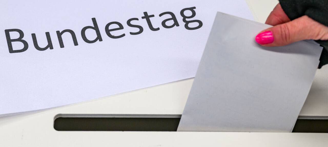 Eine Wählerin wirft in einem Wahllokal ihren Stimmzettel in eine Wahlurne, auf der ein Zettel mit der Aufschrift "Bundestag" liegt.