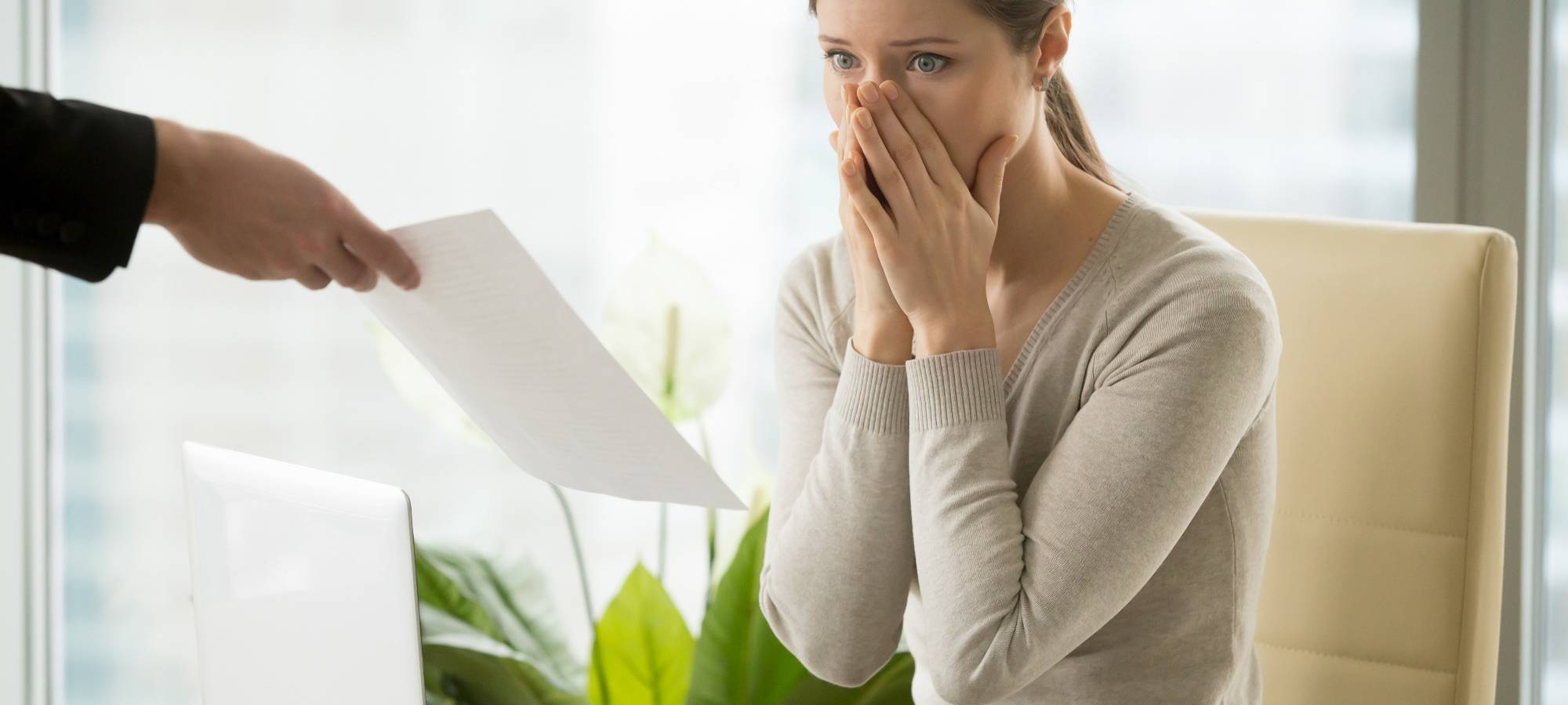Frau sitzt am Schreibtisch mit geschocktem Gesicht, erhält die Kündigung.