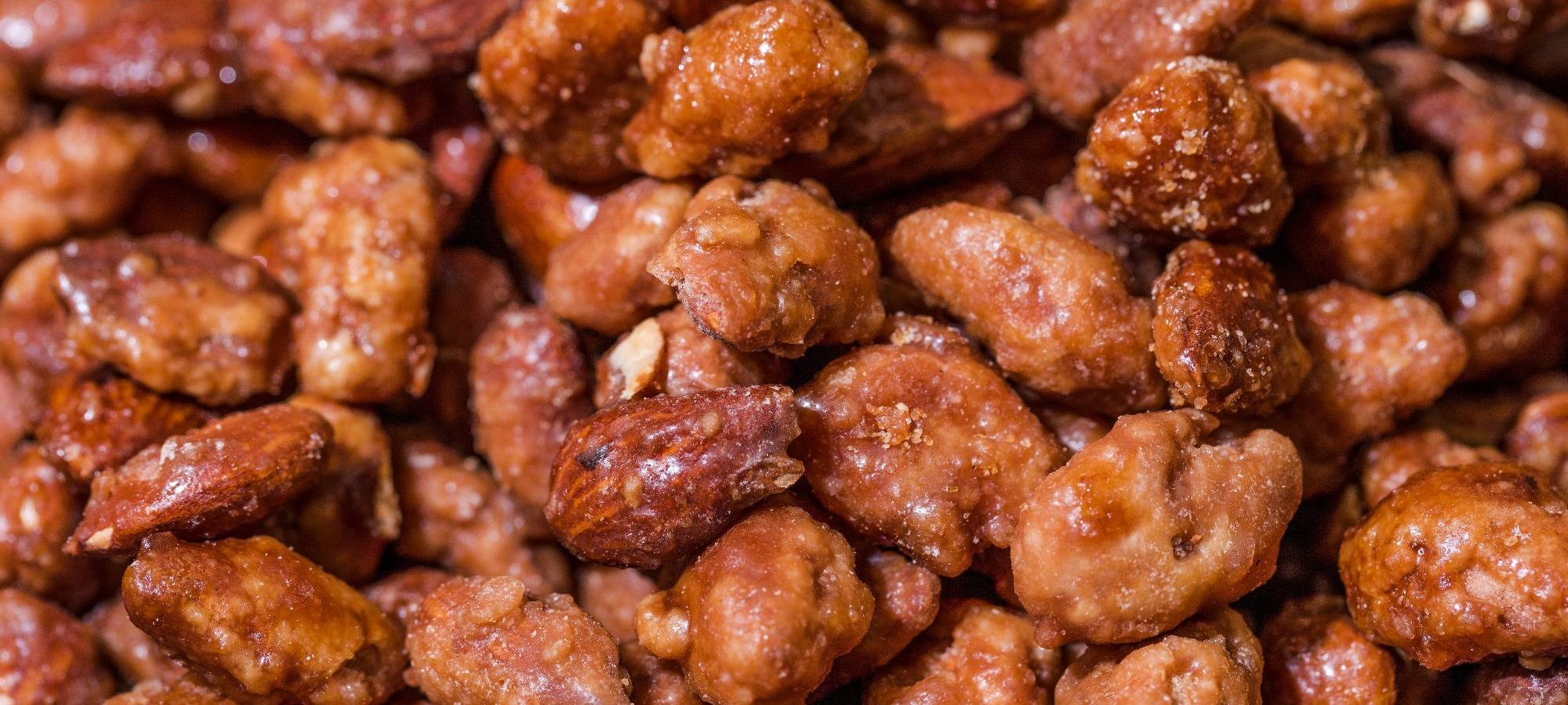 Gebrannte Mandeln liegen mit Orangenscheiben und Zimtstangen auf einer roten Decke.