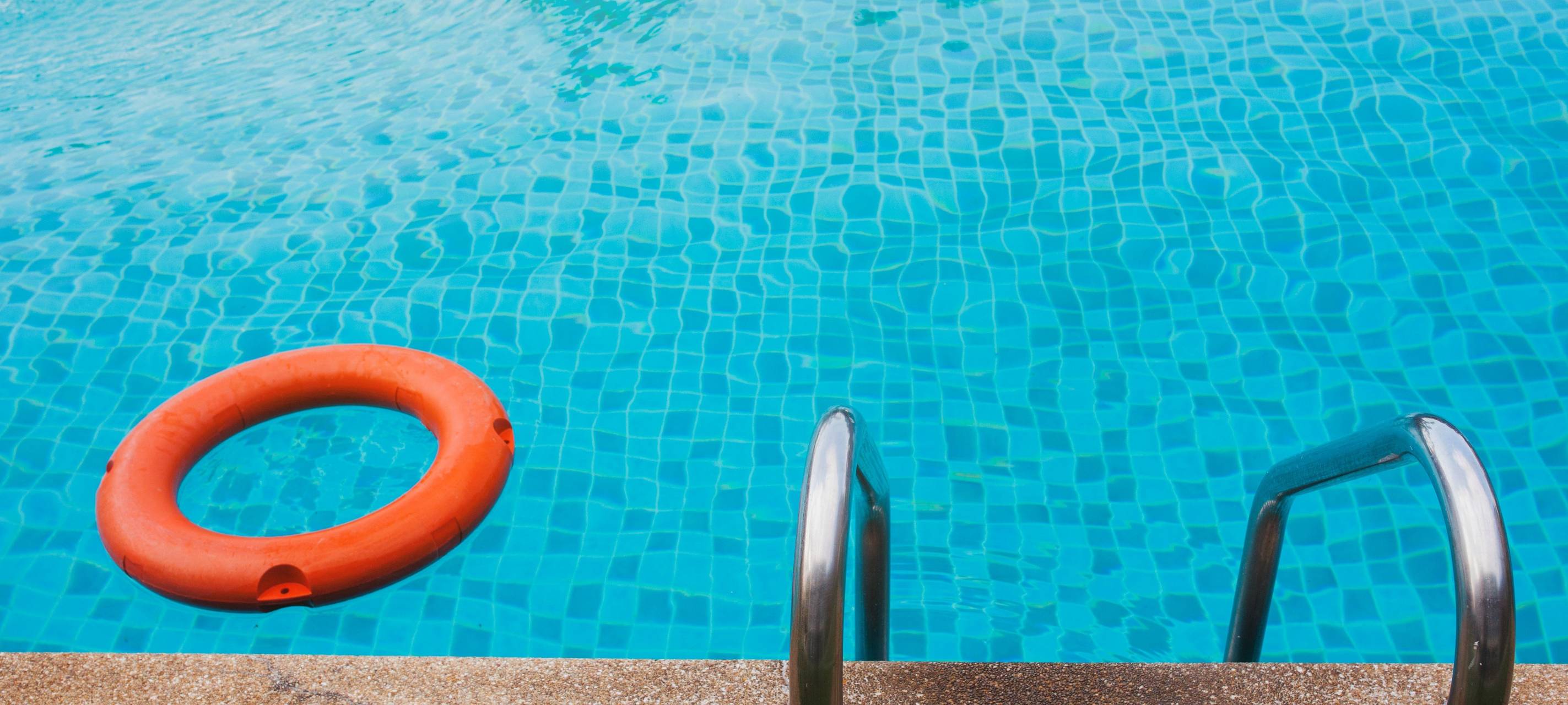 Beckenrand eines Pools in dem ein orangener Rettungsring liegt