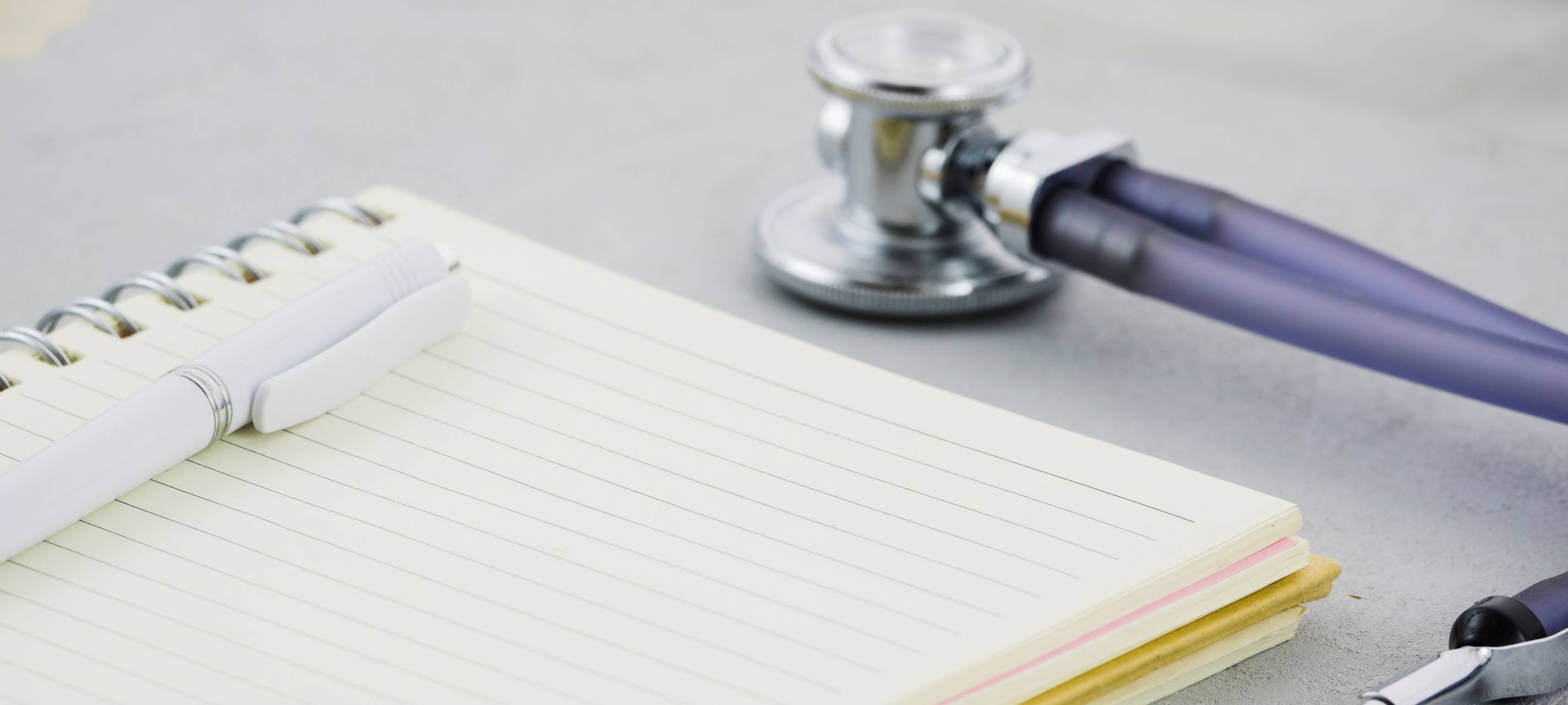 Ein Stift liegt auf einem Notizbuch. Daneben liegt ein Stethoskop