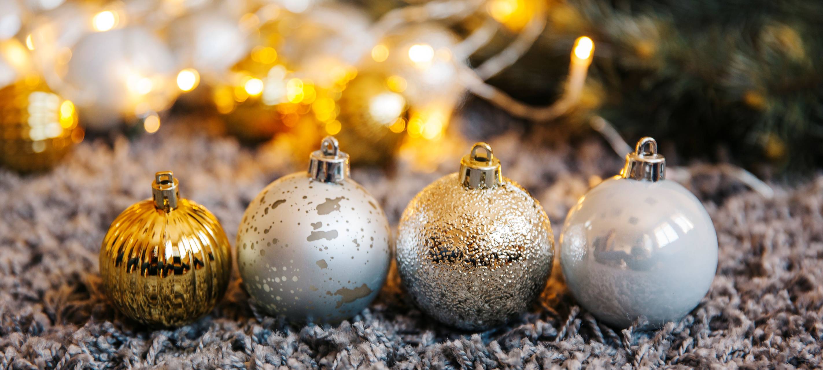 vier verschiedene Weihnachtskugeln liegen vor dem Weihnachtsbaum auf dem Teppich