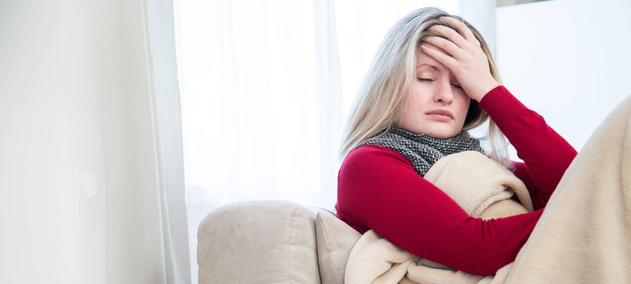 Eine Frau sitzt krank auf einem Sofa