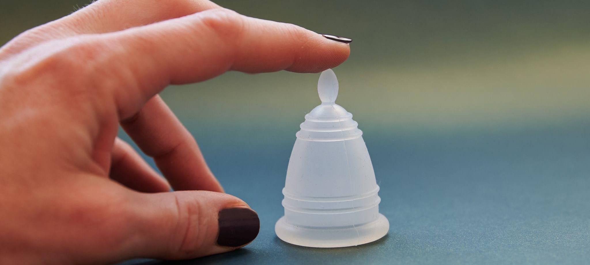 Eine Frau zeigt auf eine Menstruationstasse