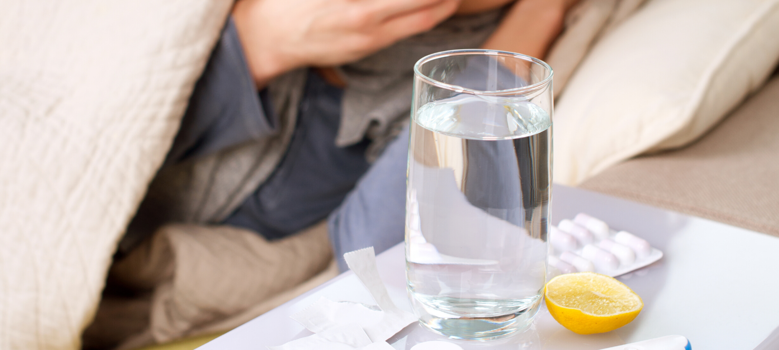 Auf dem Nachttisch einer erkälteten Person steht ein Tee und daneben liegt ein Fieberthermometer.